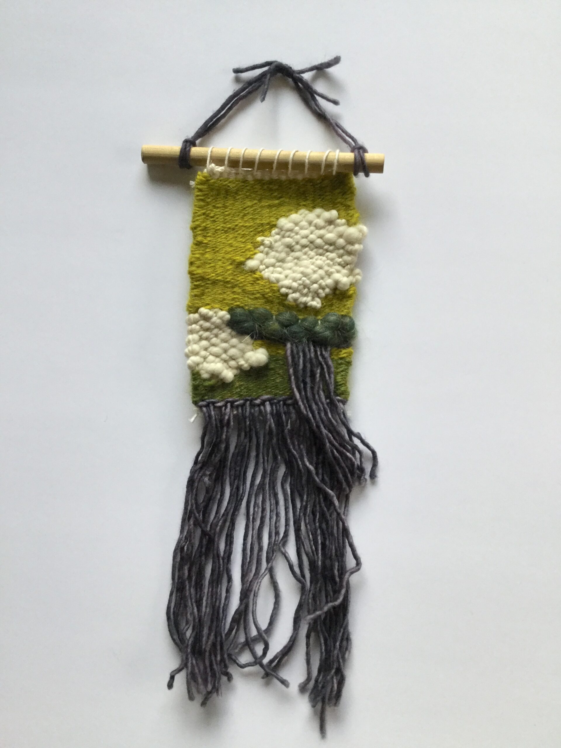 A small wooly weaving, mostly in green, with two white patches and dark gray fringe.