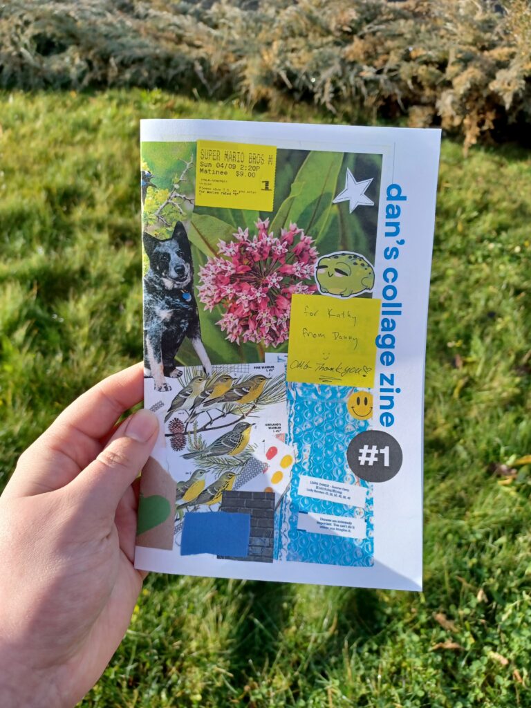 My hand holding a full size zine with the title "dan's collage zine #1" in front of a grassy background. Half of a collage is visible on the cover.