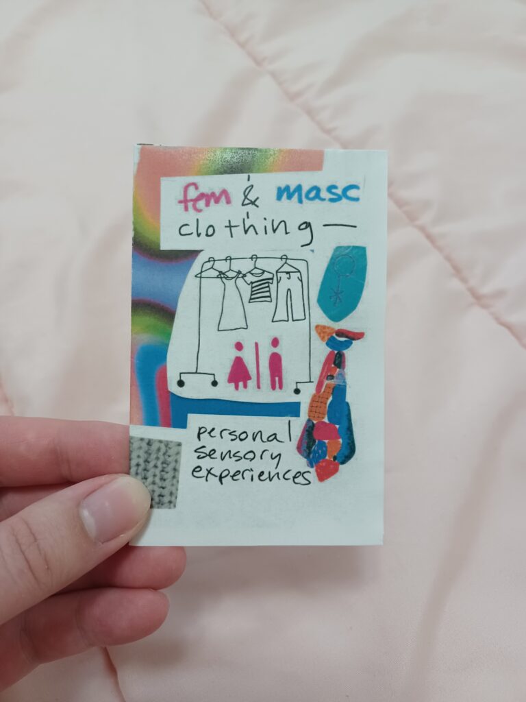My hand holding a minizine with the title "fem & masc clothing—personal sensory experiences" in front of a pink quilted background.
