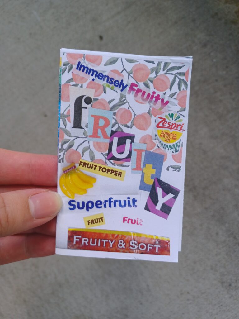My hand holding a minizine with the title "fruity" in front of a concrete background.